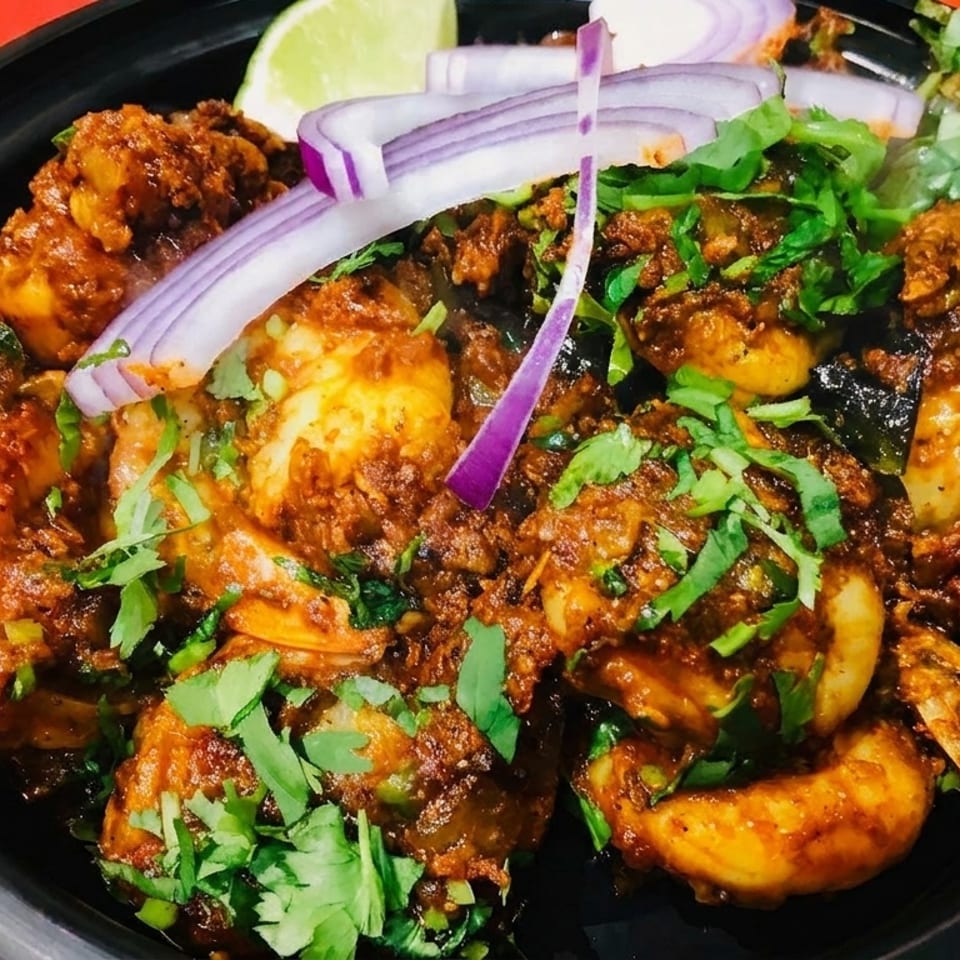 Spicy shrimp dish garnished with fresh cilantro, sliced red onions, and a lime wedge in a black bowl.