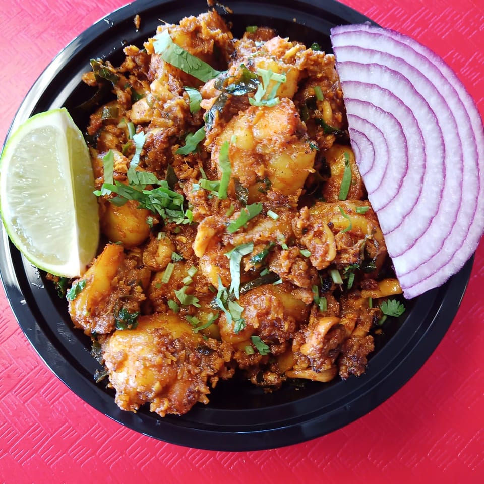 Spicy chicken dish with cilantro, a lime wedge, and red onion slices in a black bowl.