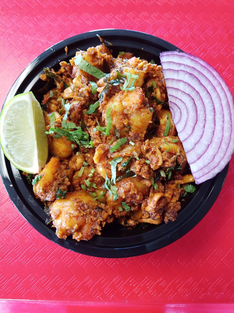 Spicy chicken dish with cilantro, a lime wedge, and red onion slices in a black bowl.