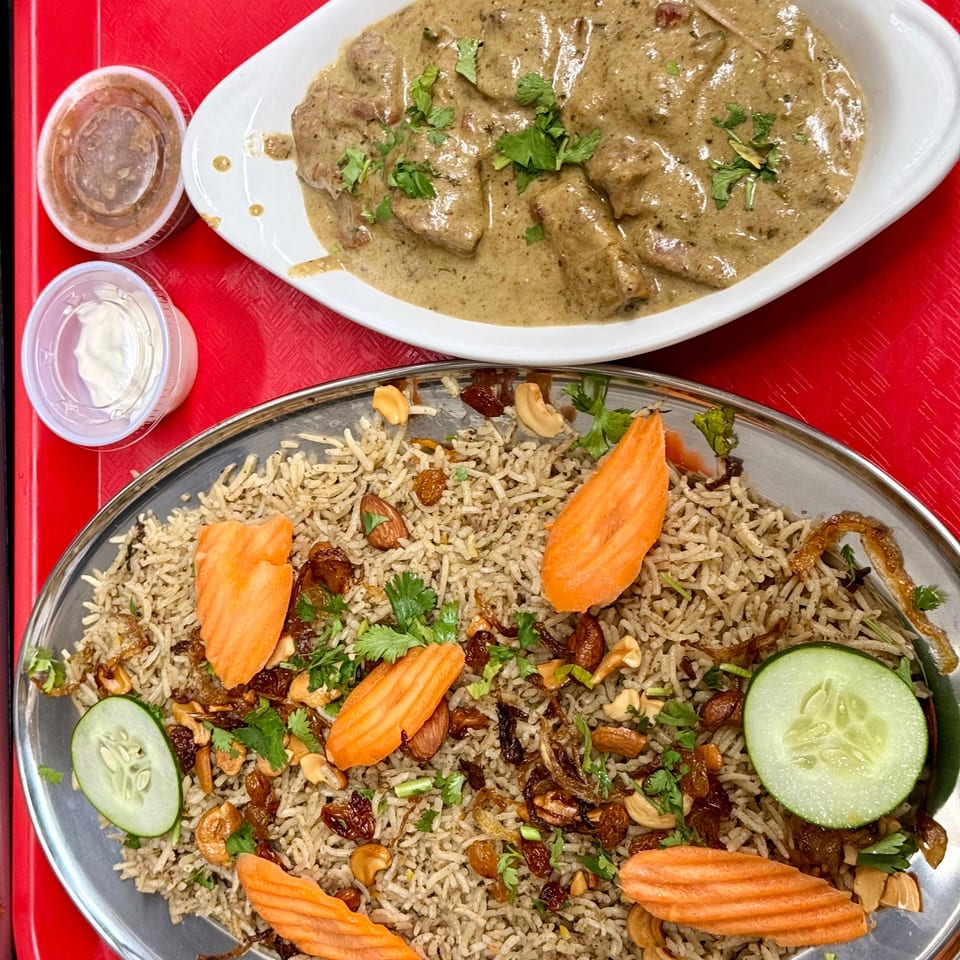 Overhead view of a red tray with a white dish of creamy meat and a metal plate of rice with nuts and vegetables.