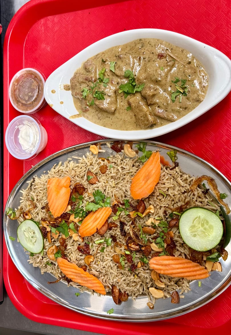 Overhead view of a red tray with a white dish of creamy meat and a metal plate of rice with nuts and vegetables.