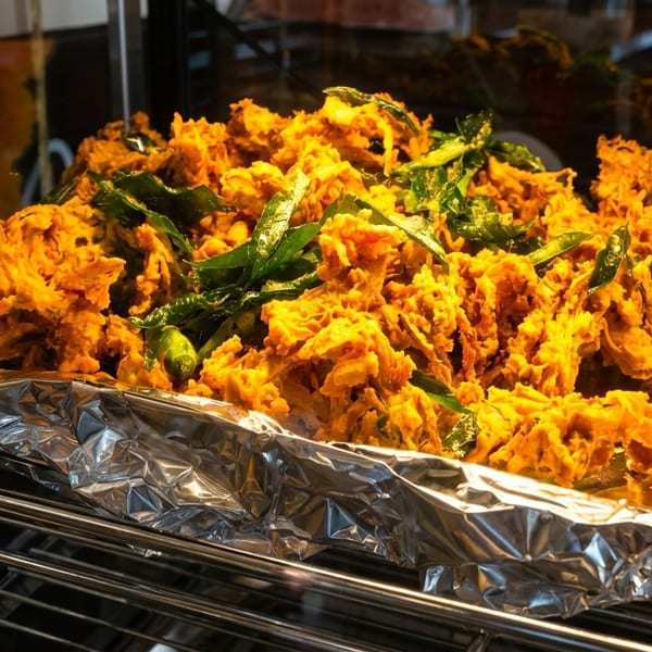 Crispy golden-brown pakoras with green herbs, served on a foil-lined tray in a warming oven.