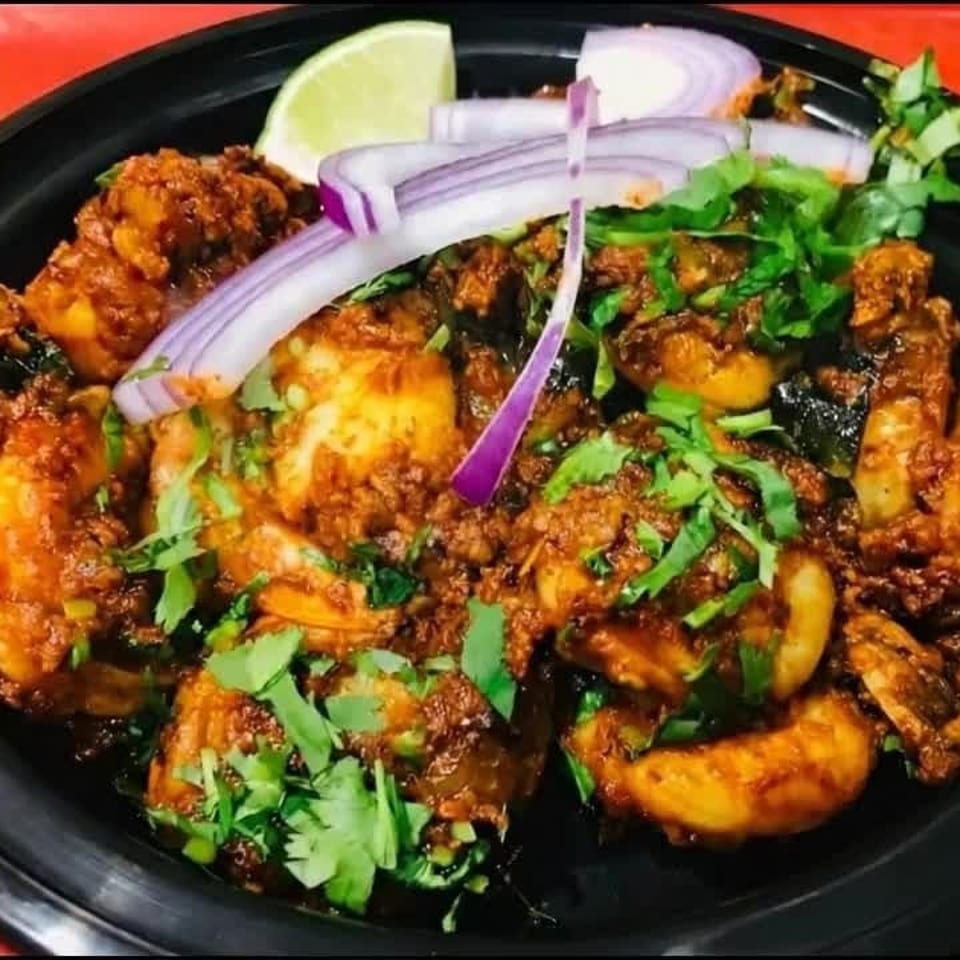 Spicy shrimp curry with cilantro, red onion, and lime in a black bowl on a red tray.