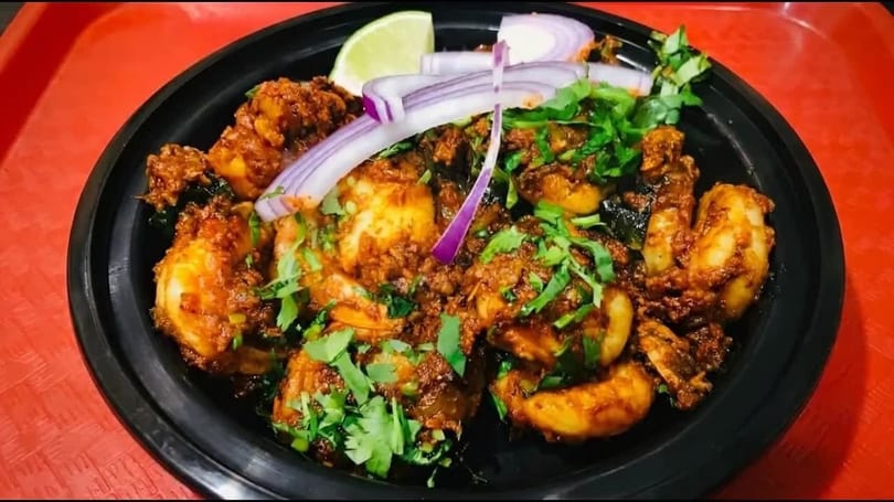 Spicy shrimp curry with cilantro, red onion, and lime in a black bowl on a red tray.