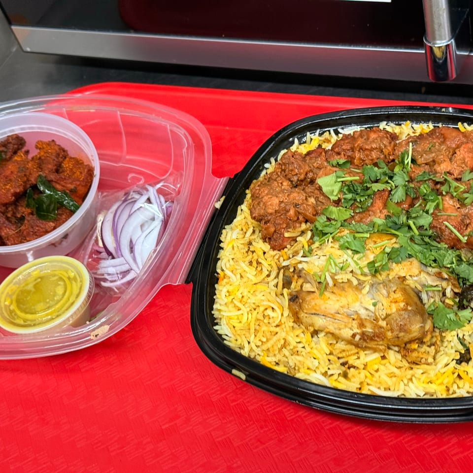 Chicken biryani with cilantro, a side of fried chicken, sliced onions, and sauces in takeout containers.