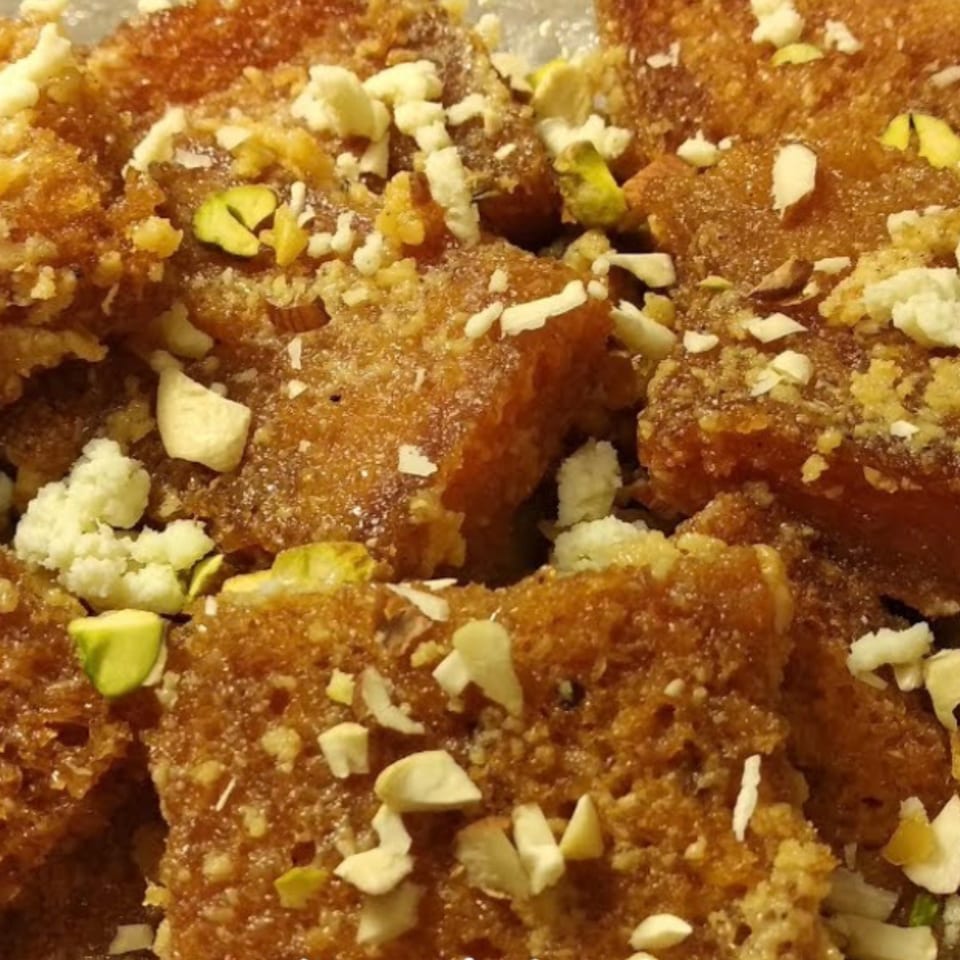 Close-up of golden-brown dessert pieces topped with white crumbles, chopped almonds, and green pistachios.