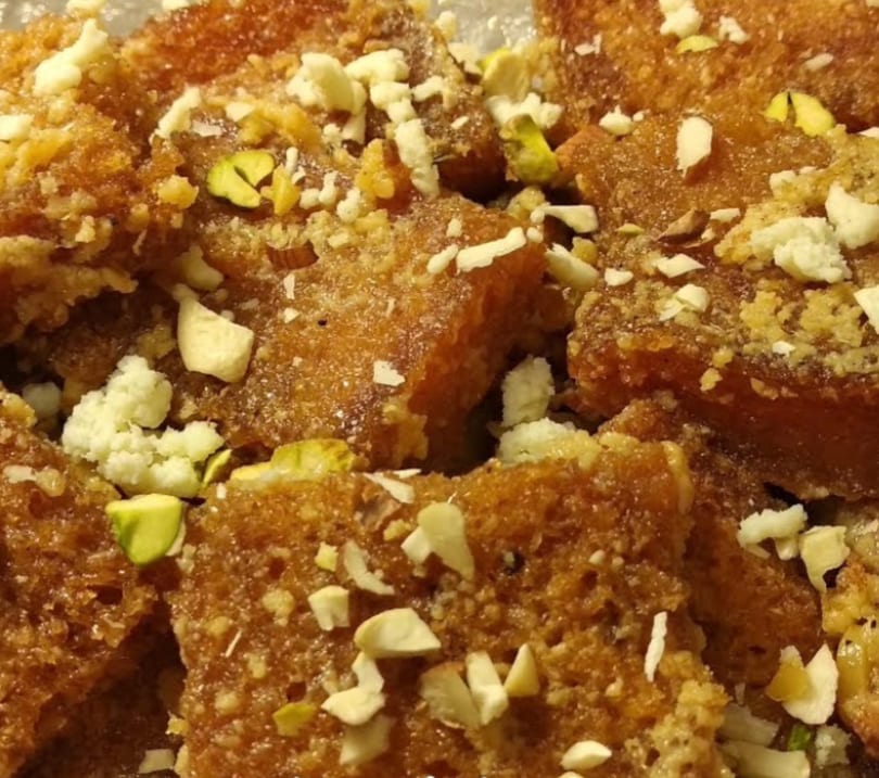 Close-up of golden-brown dessert pieces topped with white crumbles, chopped almonds, and green pistachios.
