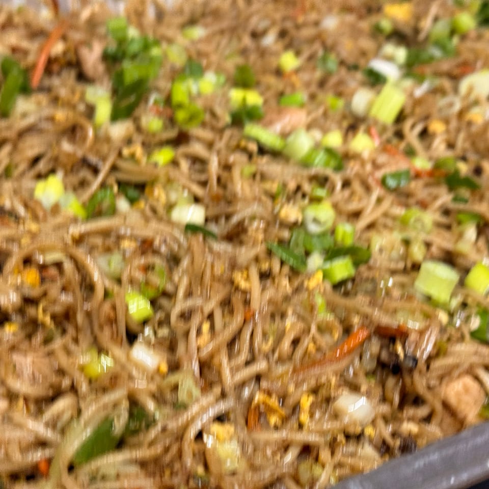 Close-up of a large tray of lo mein noodles with vegetables and green onions.
