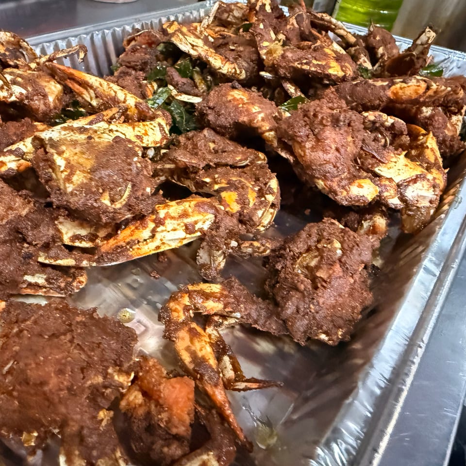 A foil tray filled with many pieces of fried crab coated in dark brown seasoning.