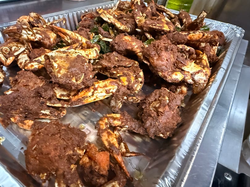 A foil tray filled with many pieces of fried crab coated in dark brown seasoning.