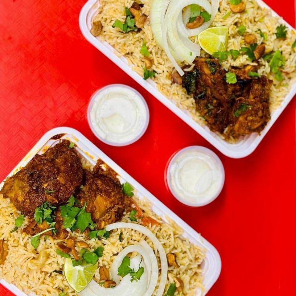Two containers of chicken biryani with rice, onions, lime, and cilantro on a red tray.