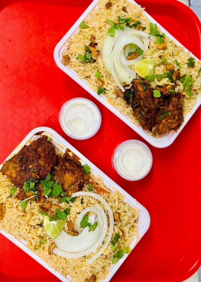 Two containers of chicken biryani with rice, onions, lime, and cilantro on a red tray.