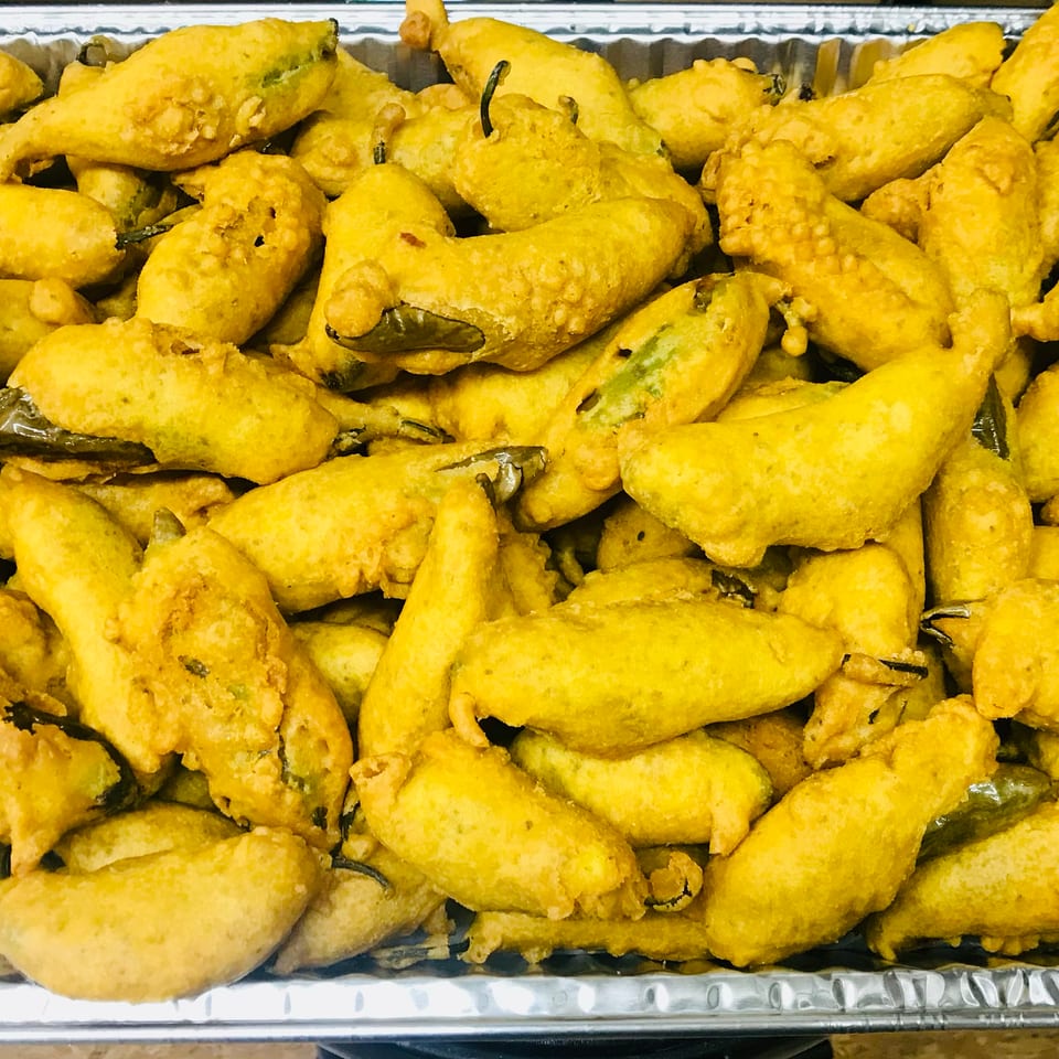 A large foil tray filled with many golden-brown, battered and fried chili peppers.
