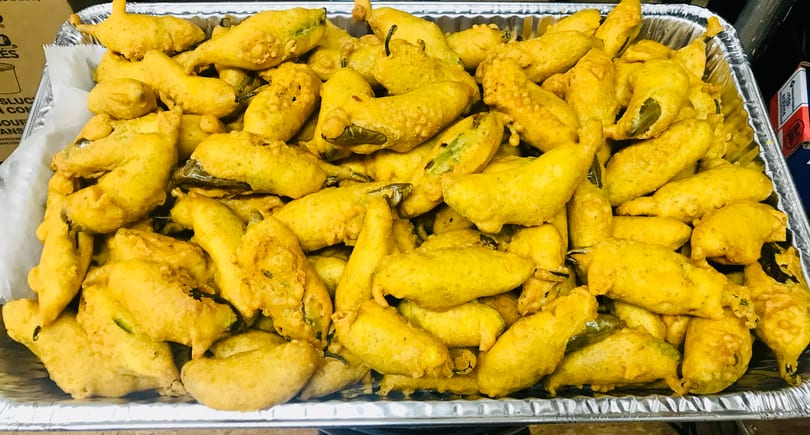 A large foil tray filled with many golden-brown, battered and fried chili peppers.