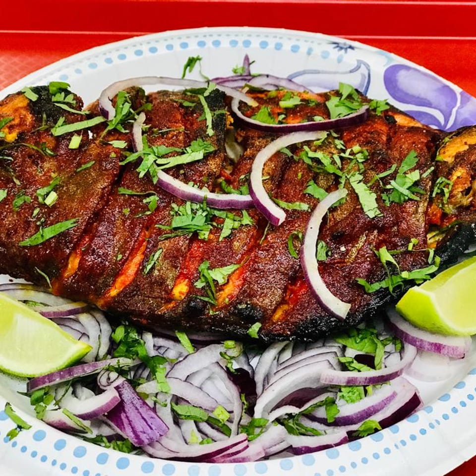 Whole grilled fish, garnished with red onion, cilantro, and lime wedges on a paper plate.