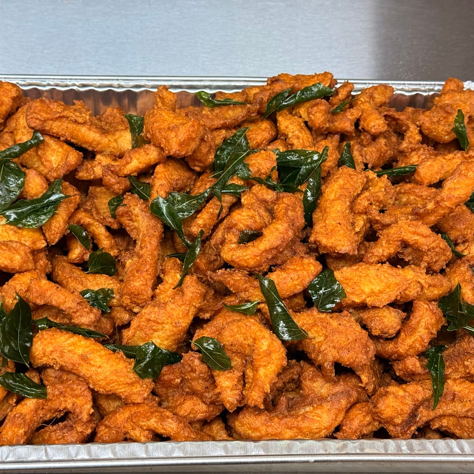 A large tray of crispy, golden-orange fried chicken pieces garnished with fresh green curry leaves.