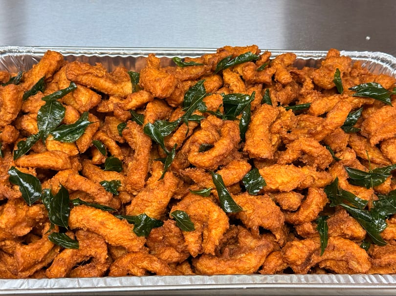 A large tray of crispy, golden-orange fried chicken pieces garnished with fresh green curry leaves.
