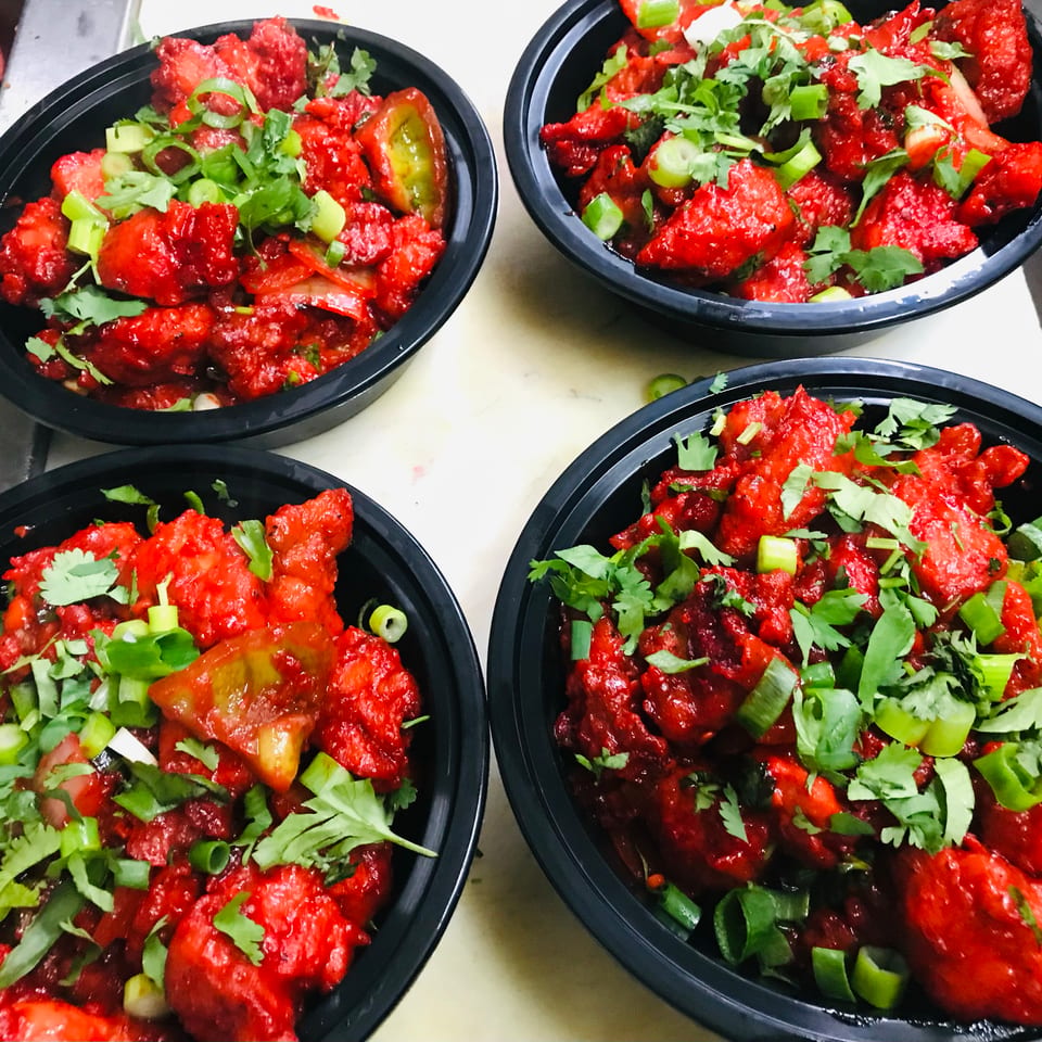 Four black bowls filled with vibrant red chili chicken, garnished with fresh cilantro and green onions.