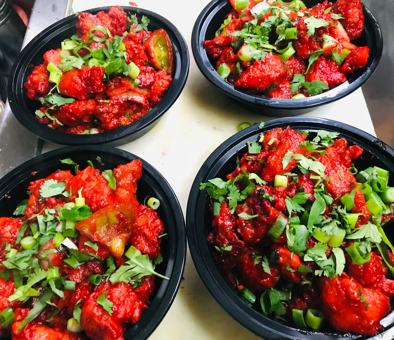 Four black bowls filled with vibrant red chili chicken, garnished with fresh cilantro and green onions.